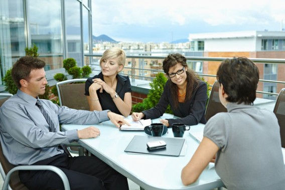 Group of young business people sitting around table on office terrace outdoor, talking and working together.