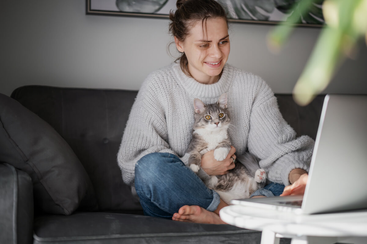 Renter searches for apartments on her computer with cat in lap. 